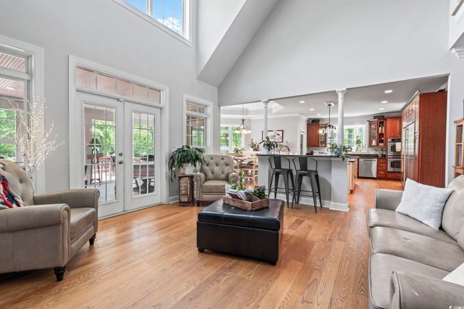 Living room featuring a towering ceiling, french doors, light wood-style floors, a chandelier, and decorative columns | Image 9