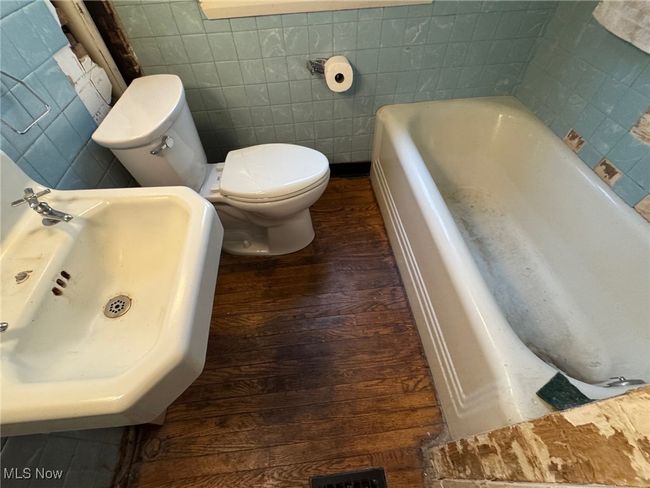 Full bathroom featuring toilet, a sink, wood finished floors, tile walls, and a bathtub | Image 18