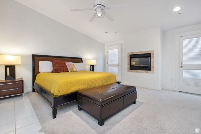 Carpeted bedroom featuring tile patterned floors, a tiled fireplace, baseboards, lofted ceiling, and ceiling fan | Image 12