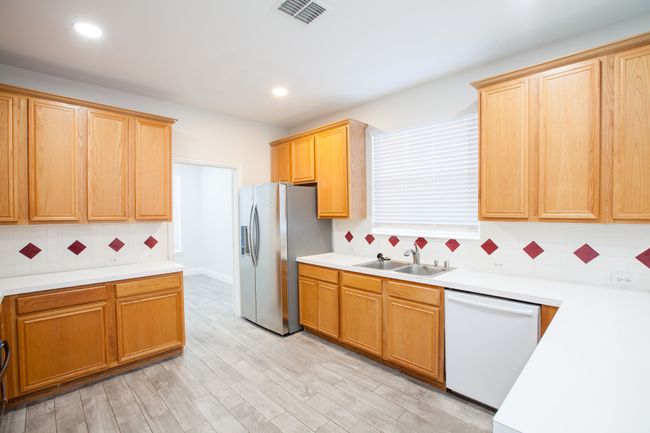 Kitchen featuring white dishwasher, stainless steel fridge, tasteful backsplash, light countertops, and light wood-style flooring | Image 11