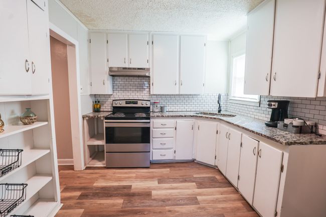 Kitchen with light wood finished floors, white cabinets, stainless steel range with electric cooktop, under cabinet range hood, and a sink | Image 8