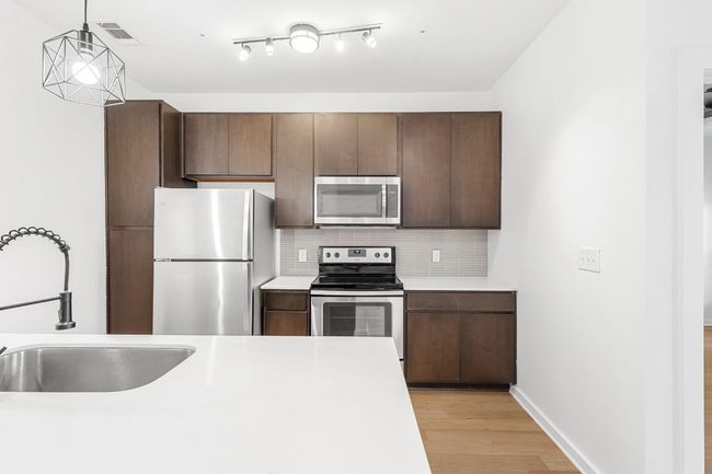 Kitchen with light wood finished floors, visible vents, decorative backsplash, appliances with stainless steel finishes, and a sink | Image 5