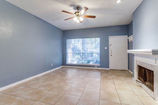 Unfurnished living room featuring a ceiling fan, a tiled fireplace, a textured ceiling, and light tile patterned flooring | Image 6