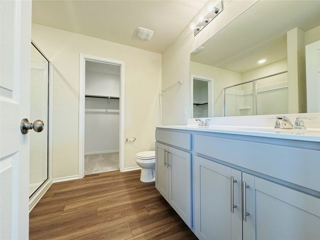 Bathroom with a stall shower, wood finished floors, double vanity, a spacious closet, and toilet | Image 17