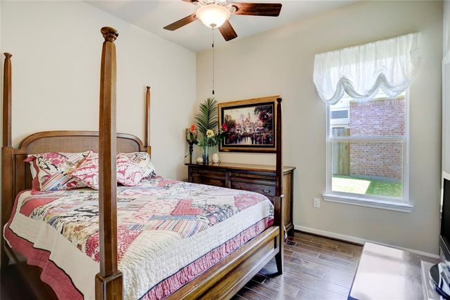 The middle secondary bedroom features a ceiling fan, hardwood flooring, and is well-lit with a warm ambiance. | Image 23