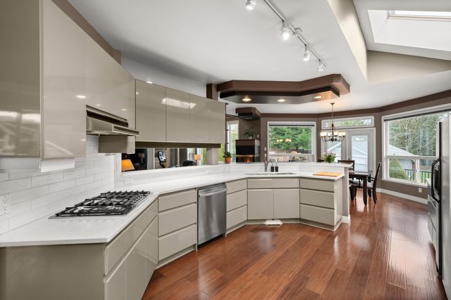 Kitchen with under cabinet range hood, a sink, dark wood finished floors, stainless steel appliances, and a peninsula | Image 15