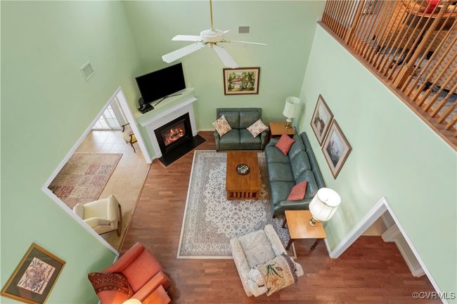 Living room featuring a high ceiling, a fireplace with flush hearth, wood finished floors, and ceiling fan | Image 31