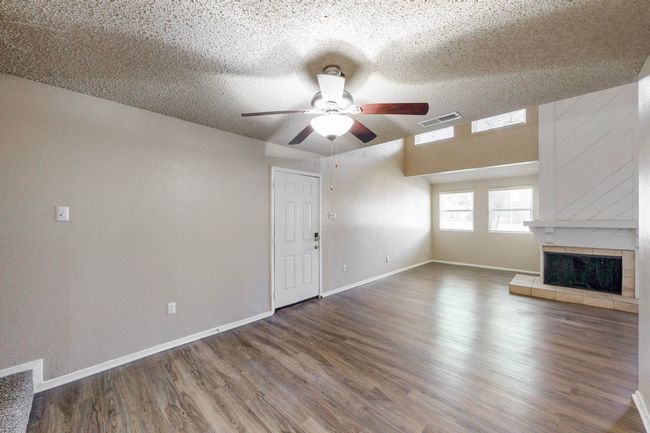 Unfurnished living room with visible vents, wood finished floors, a fireplace, baseboards, and ceiling fan | Image 15