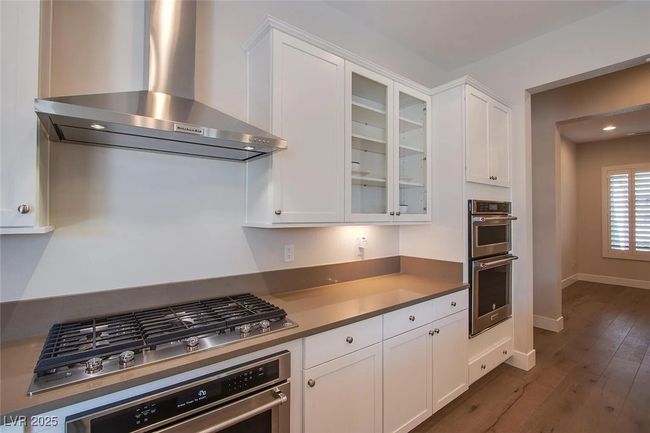 Kitchen with wall chimney range hood, white cabinetry, stainless steel appliances, and glass insert cabinets | Image 6