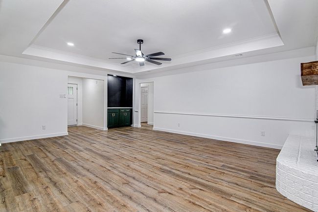 Unfurnished living room with a raised ceiling, ceiling fan, wood finished floors, baseboards, and ornamental molding | Image 10