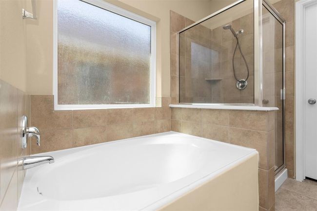 Set beneath a large frosted glass window, the oversized garden tub invites relaxation, while a nearby separate walk-in shower adds convenience for quick rinses. | Image 16