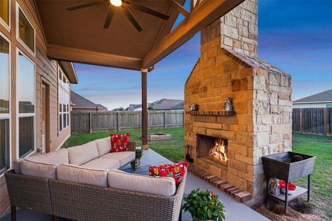 Fenced backyard featuring ceiling fan, an outdoor living space with a fireplace, and a patio area | Image 31