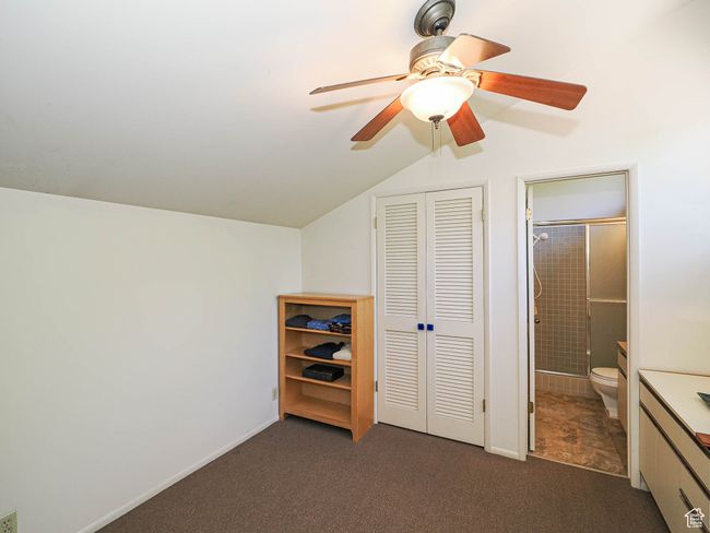 Bedroom with carpet floors, lofted ceiling, connected bathroom, a closet, and a ceiling fan | Image 39