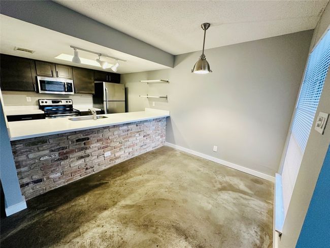 Kitchen with concrete flooring, appliances with stainless steel finishes, a textured ceiling, decorative light fixtures, and track lighting | Image 6