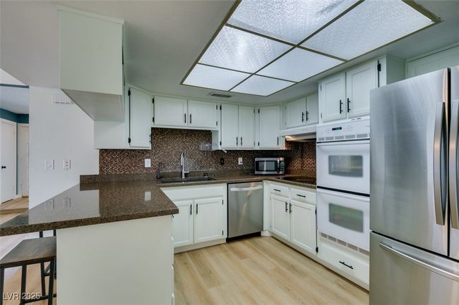 Kitchen with appliances with stainless steel finishes, a peninsula, light wood finished floors, under cabinet range hood, and dark stone countertops | Image 25