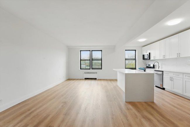 Kitchen featuring radiator heating unit, light wood-type flooring, stainless steel appliances, light countertops, and white cabinets | Image 10