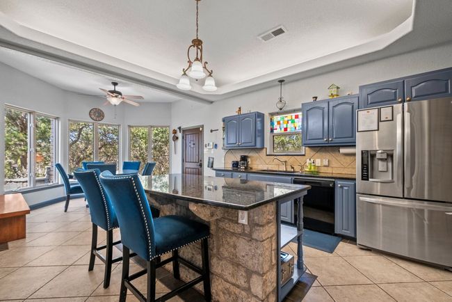 Kitchen with black dishwasher, stainless steel refrigerator with ice dispenser, visible vents, backsplash, and a kitchen bar | Image 11