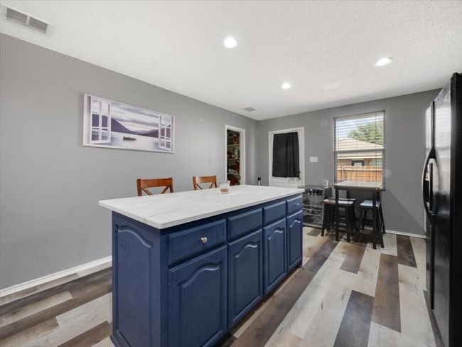 Kitchen featuring light hardwood / wood-style floors, black fridge, blue cabinets, a textured ceiling, and a center island | Image 12