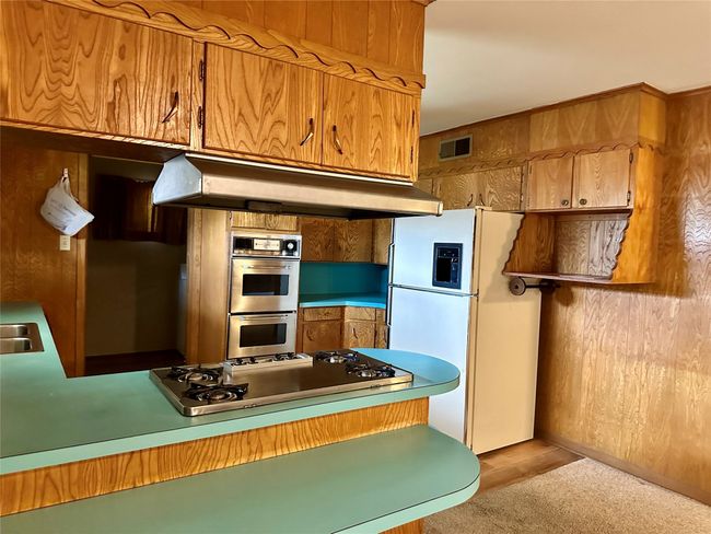 Kitchen with visible vents, under cabinet range hood, stovetop, freestanding refrigerator, and stainless steel double oven | Image 6