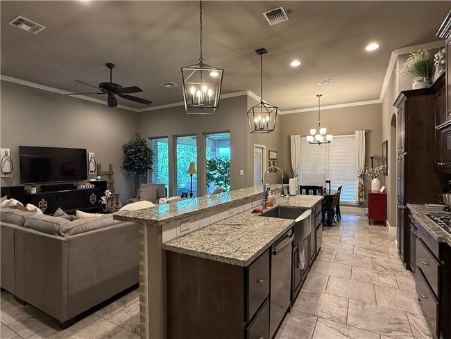 Kitchen featuring a ceiling fan, dark brown cabinets, ornamental molding, a kitchen island with sink, and a chandelier | Image 9