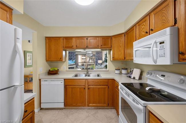 Kitchen with white appliances, light tile patterned flooring, and sink | Image 8