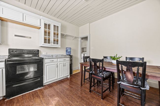 Kitchen with black range with electric stovetop, dark wood-type flooring, glass insert cabinets, and white cabinetry | Image 14