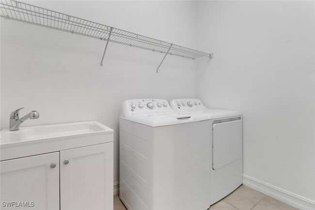 Laundry area featuring washing machine and dryer, light tile patterned flooring, cabinet space, and baseboards | Image 9