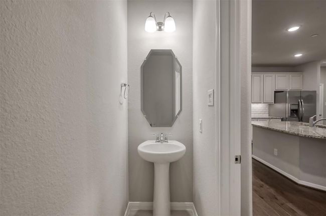 Half-bath with pedestal sink and mirror, well-lit, located conveniently near the kitchen and dining area for easy guest access. | Image 13