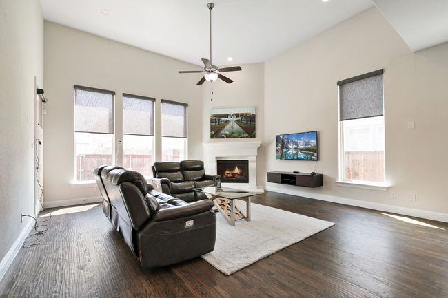 Living room featuring a warm lit fireplace, dark wood-style floors, baseboards, and ceiling fan | Image 14