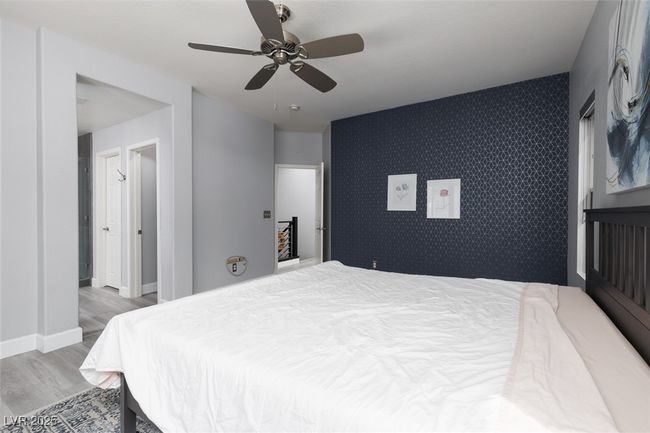 Bedroom featuring a ceiling fan, an accent wall, wood finished floors, wallpapered walls, and baseboards | Image 22