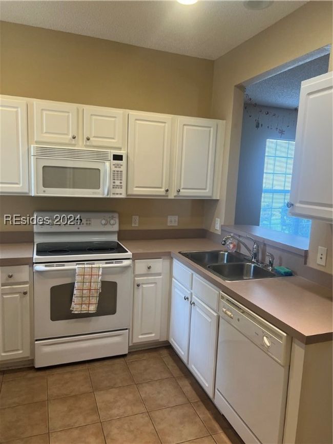 Kitchen featuring white dishwasher, stove, white cabinetry, and light tile patterned flooring | Image 13