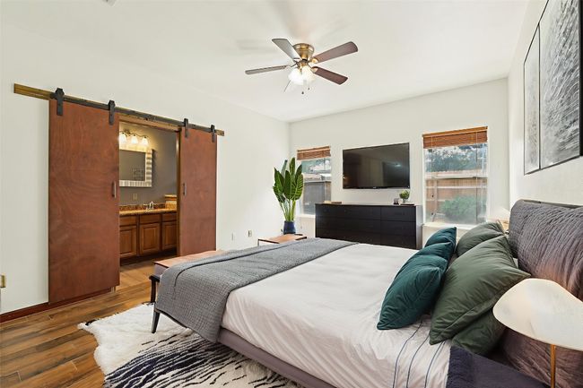 Bedroom with a barn door, wood finished floors, connected bathroom, and a ceiling fan | Image 9
