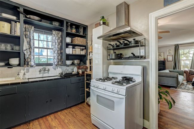 Kitchen with open shelves, wall chimney exhaust hood, white gas range oven, and a sink | Image 11