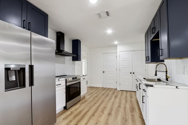 Kitchen with visible vents, white cabinets, wall chimney exhaust hood, stainless steel appliances, and light countertops | Image 9