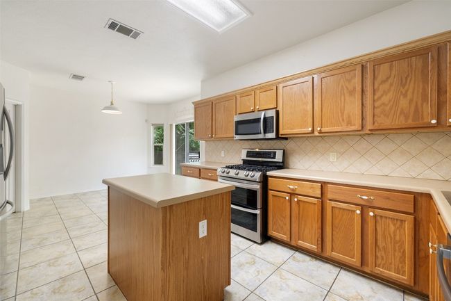 Kitchen with appliances with stainless steel finishes, decorative backsplash, visible vents, and a center island | Image 14