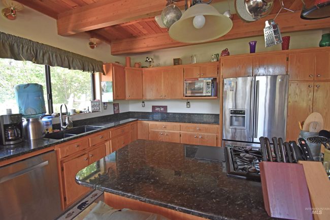 Kitchen with appliances with stainless steel finishes, a wood ceiling with exposed beams, brown cabinets, and dark stone counters | Image 46
