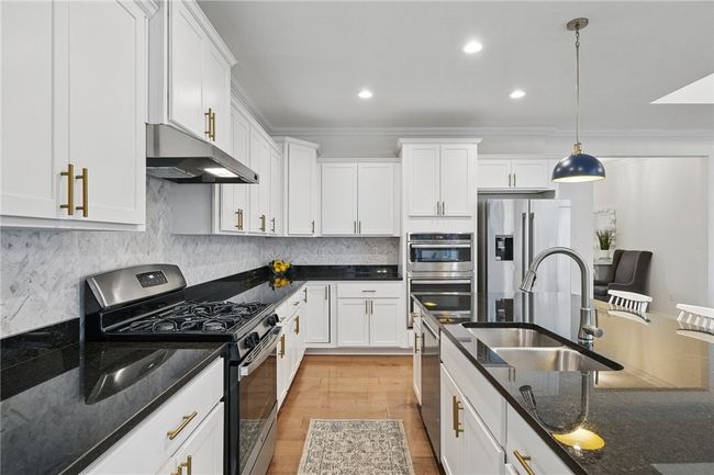 Gourmet kitchen seamlessly connected to the great room, featuring white cabinetry, granite countertops, stainless steel appliances, and a spacious island with pendant lighting. Open-concept layout provides a perfect flow for entertaining and everyday living. | Image 14