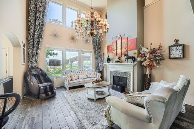 Living room with arched walkways, a towering ceiling, a fireplace, wood finished floors, and a chandelier | Image 6