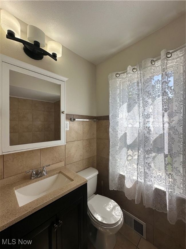 Bathroom featuring tile patterned flooring, tile walls, toilet, vanity, and visible vents | Image 25
