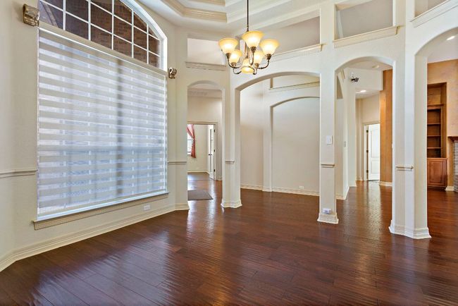 Unfurnished dining area with a towering ceiling, an inviting chandelier, wood finished floors, and arched walkways | Image 4