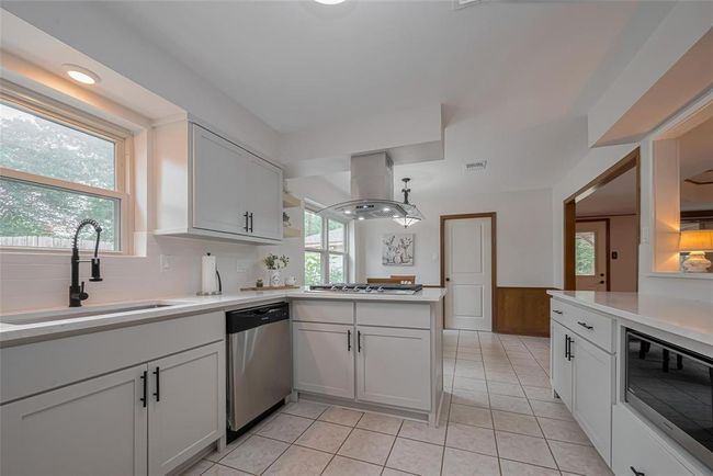 This modern kitchen features sleek white cabinetry with natural light streaming through a window above the sink. | Image 19