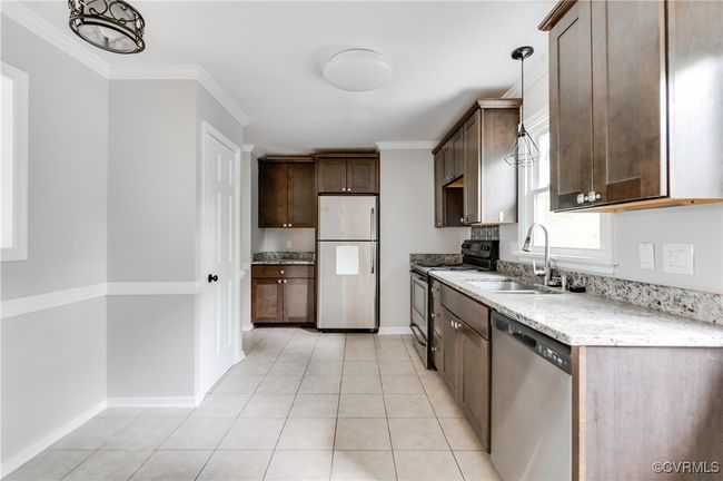 Kitchen featuring stainless steel appliances, dark brown cabinetry, crown molding, decorative light fixtures, and light tile patterned flooring | Image 7