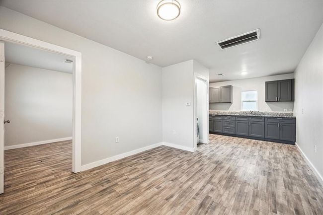 This photo showcases a modern, open-concept space with light wood flooring and neutral walls. It includes a kitchen area with sleek dark cabinets and granite countertops. A doorway leads to an additional room, offering flexibility for a bedroom or office. Natural light enters through a small window, enhancing the bright and airy feel. | Image 10