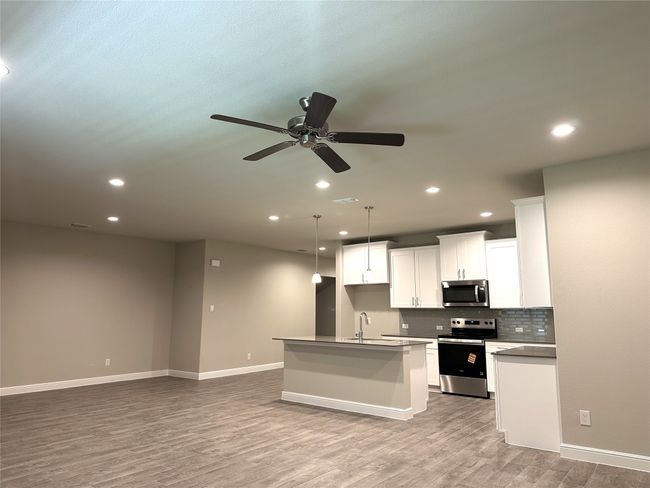 Kitchen with appliances with stainless steel finishes, light wood-style floors, an island with sink, backsplash, and open floor plan | Image 4