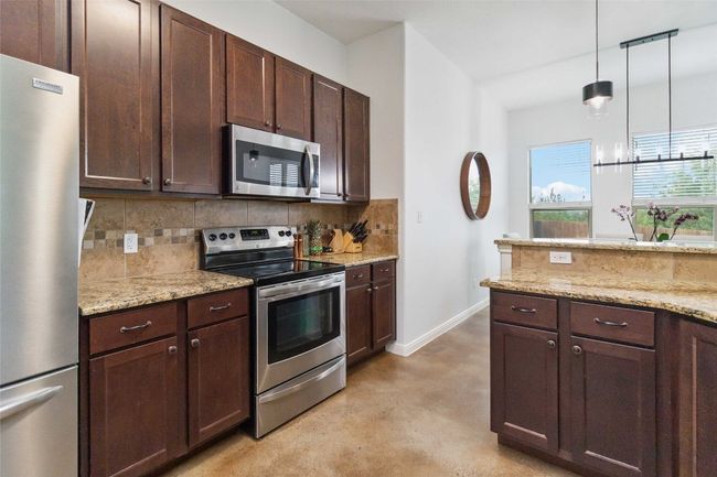 Kitchen featuring appliances with stainless steel finishes, backsplash, finished concrete floors, dark brown cabinets, and hanging light fixtures | Image 14
