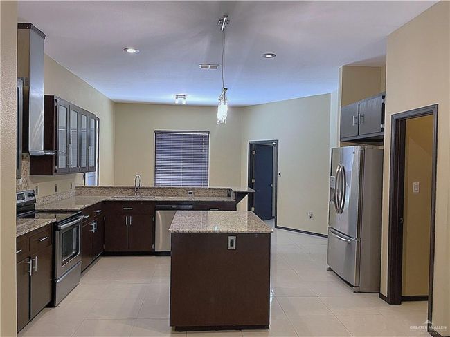 Kitchen with stainless steel appliances, a sink, a peninsula, dark brown cabinetry, and light stone counters | Image 8