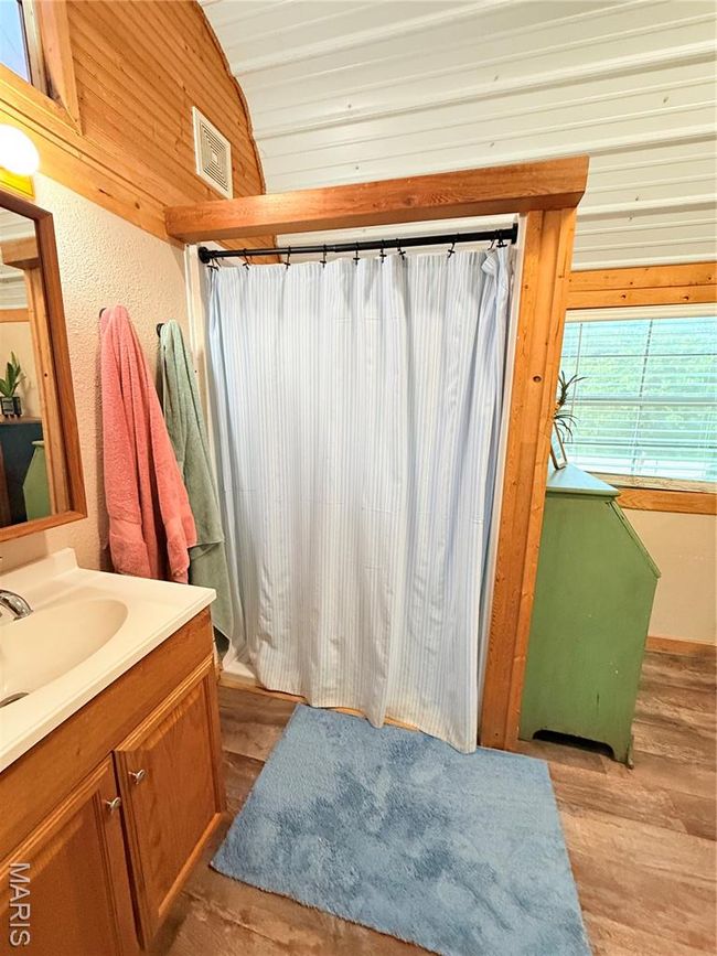 Bathroom featuring wood finished floors, vanity, lofted ceiling, a shower with curtain, and wooden walls | Image 17