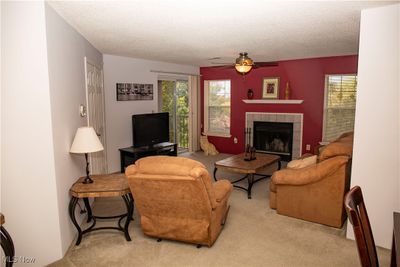 Carpeted living room with ceiling fan, a tiled fireplace, and a textured ceiling | Image 2