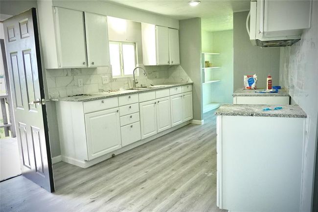 Kitchen featuring light wood finished floors, white cabinets, backsplash, a sink, and baseboards | Image 6