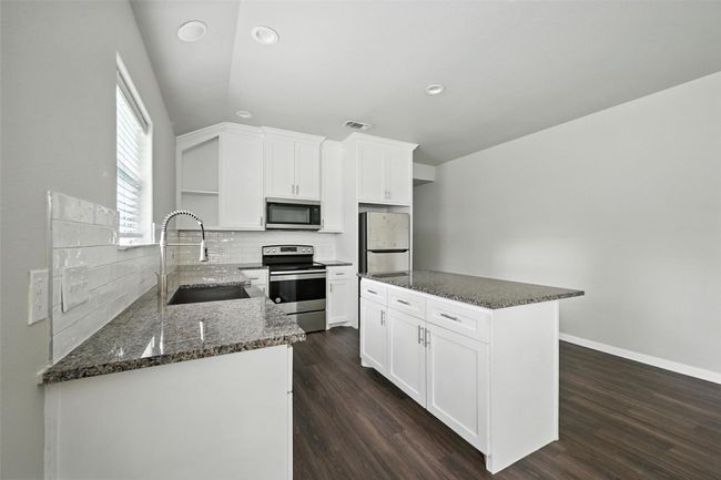Kitchen featuring stainless steel appliances, dark stone countertops, white cabinets, dark wood finished floors, and tasteful backsplash | Image 4